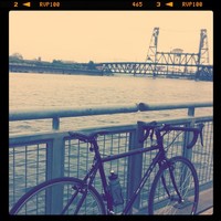 Bicycle leaning against a dock railing on the Willamette River, with the Steel Bridge in the background. Filtered to appear like a faded slide