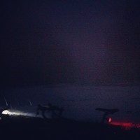 Extremely dark photo taken at Council Crest park in the snow, late at night. The headlight and tail light of a bicycle are visible