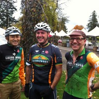 Casual portrait, three men in their late 30s/early 40s wearing coordinated “Team Oregon presented by Laurelwood” bicycle racing kit, next to a wet bicycle racing venue