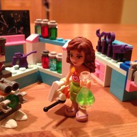 Closeup of a Lego Friends minidoll in a laboratory, holding a beaker, standing next to a small robot