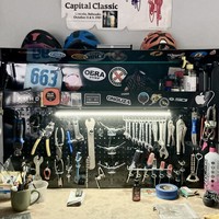 Workbench in a home bike shope with magnetic pegboard, thick with a motley assortment of tools. The workbench is covered with bicycle and outdoor sports-related stickers