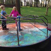 Three young kids with mudy boots, on a rusty old merry go round at a tree filled park