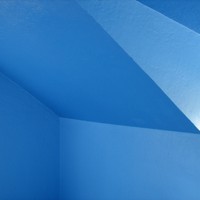 Abstractly composed photo of the blue-painted walls and ceiling in a dormer bedroom. no objects are visible, only the angles of the blue walls and ceiling intersecting and reflecting light in an ambiguous manner