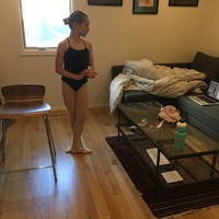 Indoors, TV den, school age girl in a leotard standing at first position, watching an instructor on a laptop