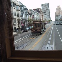 Shot out of the back of a cable car up a steep San Francisco Street; a woman’s face and hair is faintly visible in the near foreground looking out the window