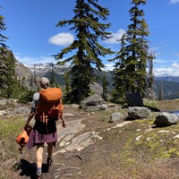 Somen wearing a backpack walking along a broad ridge with lightly glaciated peaks on the horizon