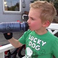 Sweaty young kid with bike gloves, in a Lucky Dog t-shirt, drinking from a bike bottle