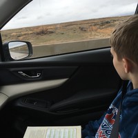 School age boy with a book on his lap, looking out the window at a dry Idaho landscape