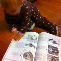 A baby in footie jams seated on the floor paging through an illustrated bicycle repair manual