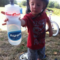 Preschool age child in a bike helmet, handing a water bottle toward the photographer