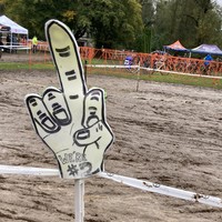 handmade sign at a very muddy cyclocross race, showing a raised middle finger and the text “we’re #2”