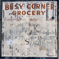 Faded commercial sign from a neighborhood convenience store, long-since closed, reading “BUSY CORNER GROCERY since 1910” followed by a mostly-illegible list of product that includes “Helium,” “Wine,” and “Gift Baskets”