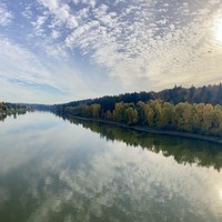 Panorama looking south up the Willamette River from a bridge about 200' above the water. The glassy river reflects a strangely greenish blue sky speckled with high altitude clouds. On the east bank is a marina, houseboats, and a condo complex. On the west bank are hills forested with dark firs and a few red maples; along the shore poplars and cottonwoods are bright yellow with fall foliage. The afternoon sun is low in the sky and shines weakly through the veil of clouds