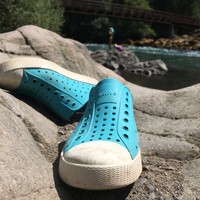 Closeup of a pair of kids’ water shoes on a rock at the side of a river