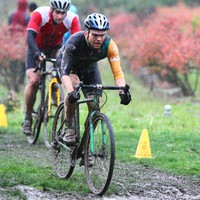Wet and muddy cyclocross bicycle racers cycling past blueberry bushes in a heavy rain