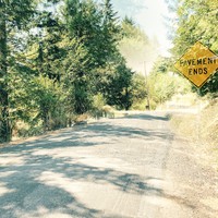 Composite photo resembling an old-fashioned double exposure, of a road sign reading “PAVEMENT ENDS” superimposed over a gravel road leading into light woods